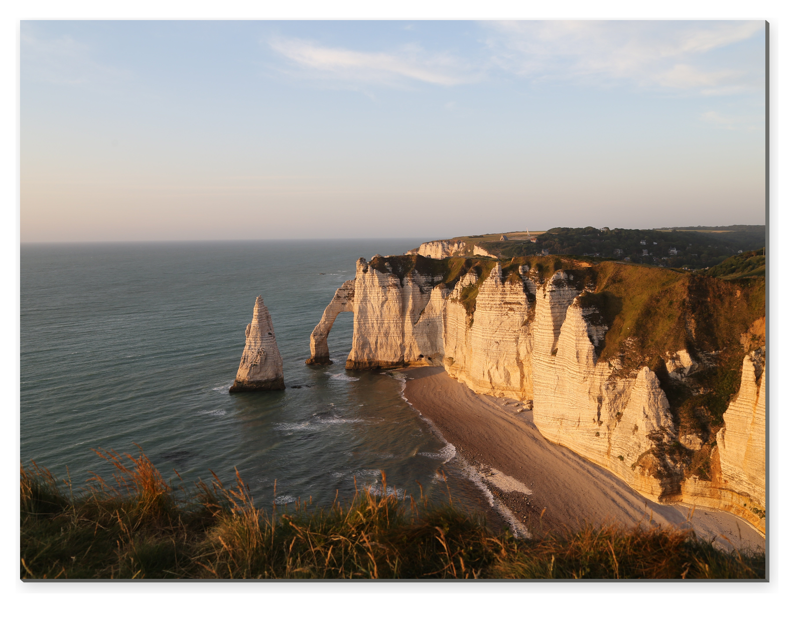 Křídové útesy Étretat se skalním obloukem a mořským jehlanem v teplém večerním světle